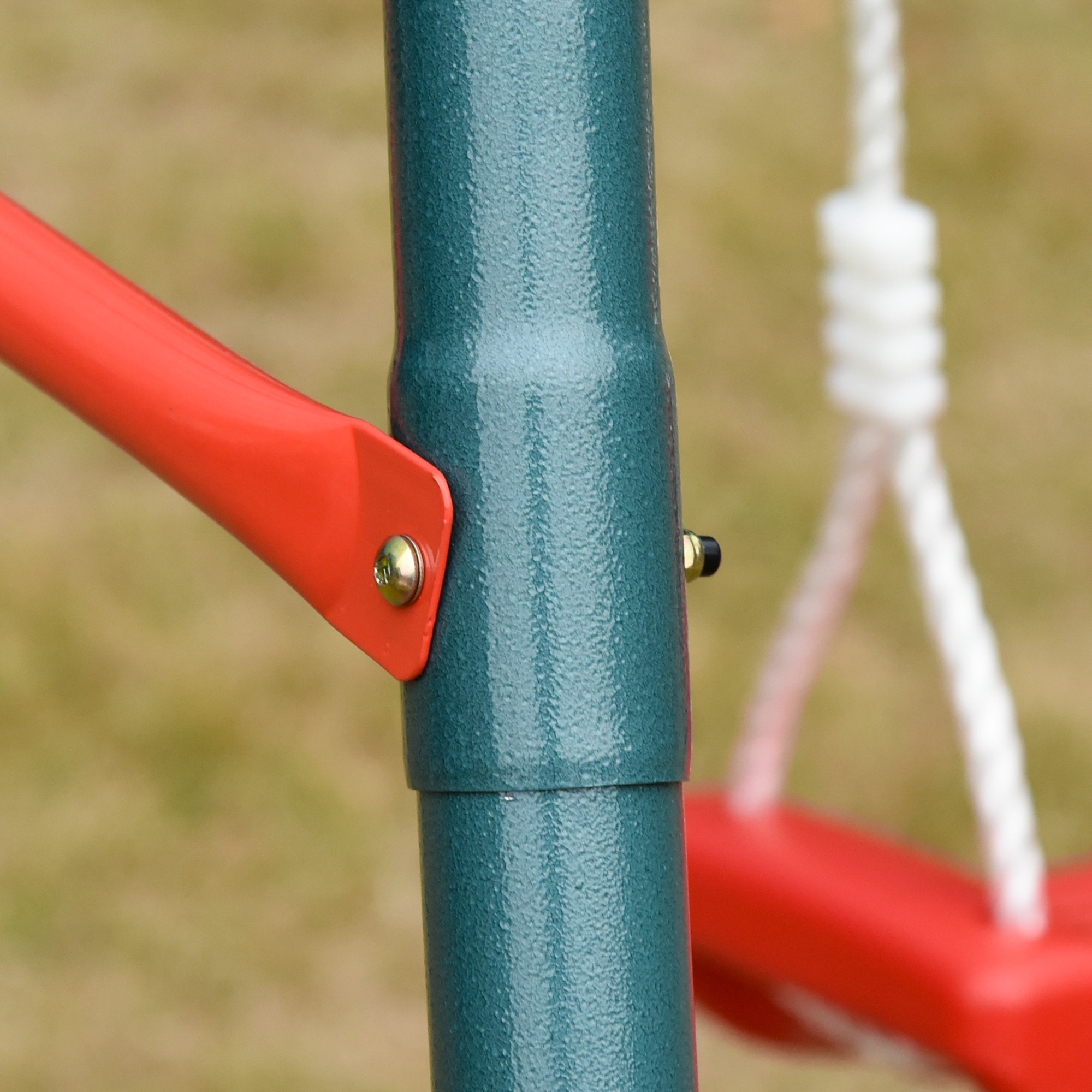 Primer plano de un columpio. Poste de metal verde azulado con soporte rojo. Cuerda blanca y asiento de columpio rojo borroso en el fondo.