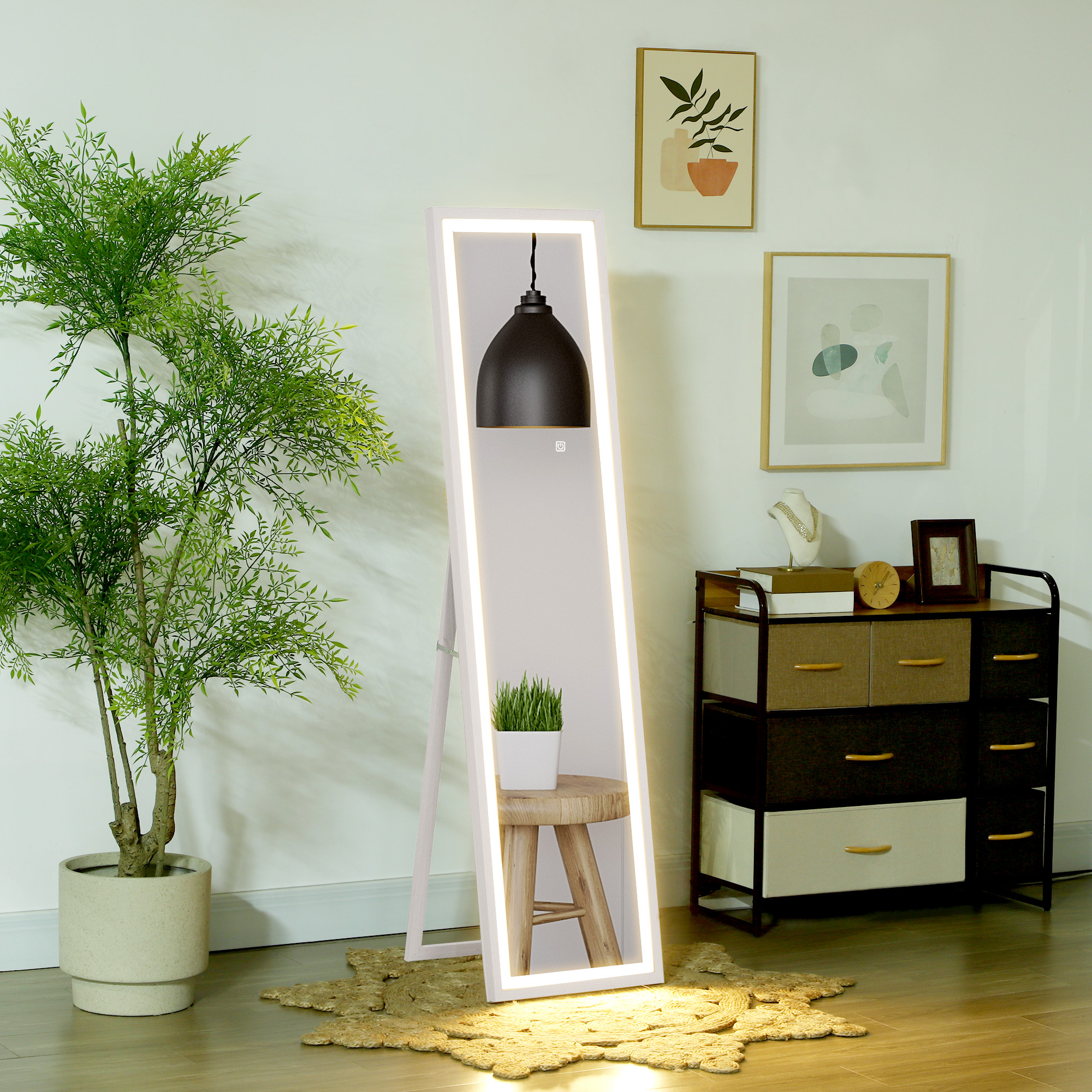 Una habitación con espejo, planta y cómoda. El espejo refleja una lámpara negra y un taburete. Hay cuadros en la pared.