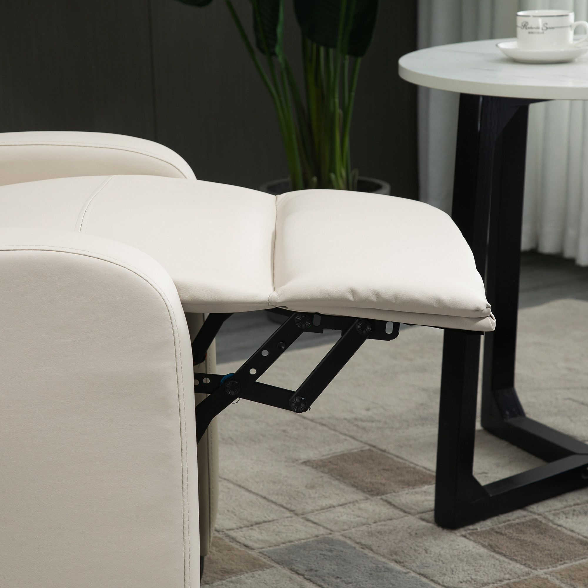 Sillón reclinable color crema con reposapiés extendido. Una mesita con taza y platillo visible en el fondo.