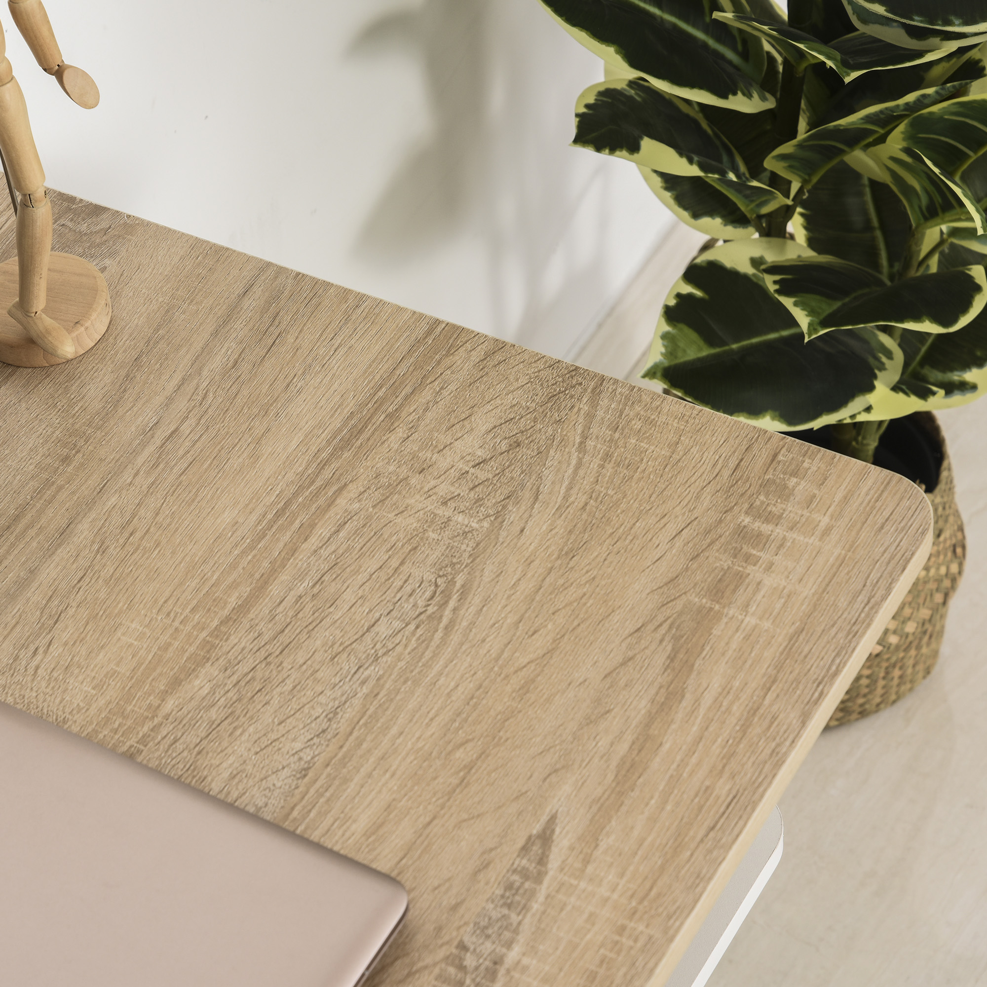 Escritorio de madera con portátil, maniquí de madera y planta en maceta con hojas verdes y amarillas.