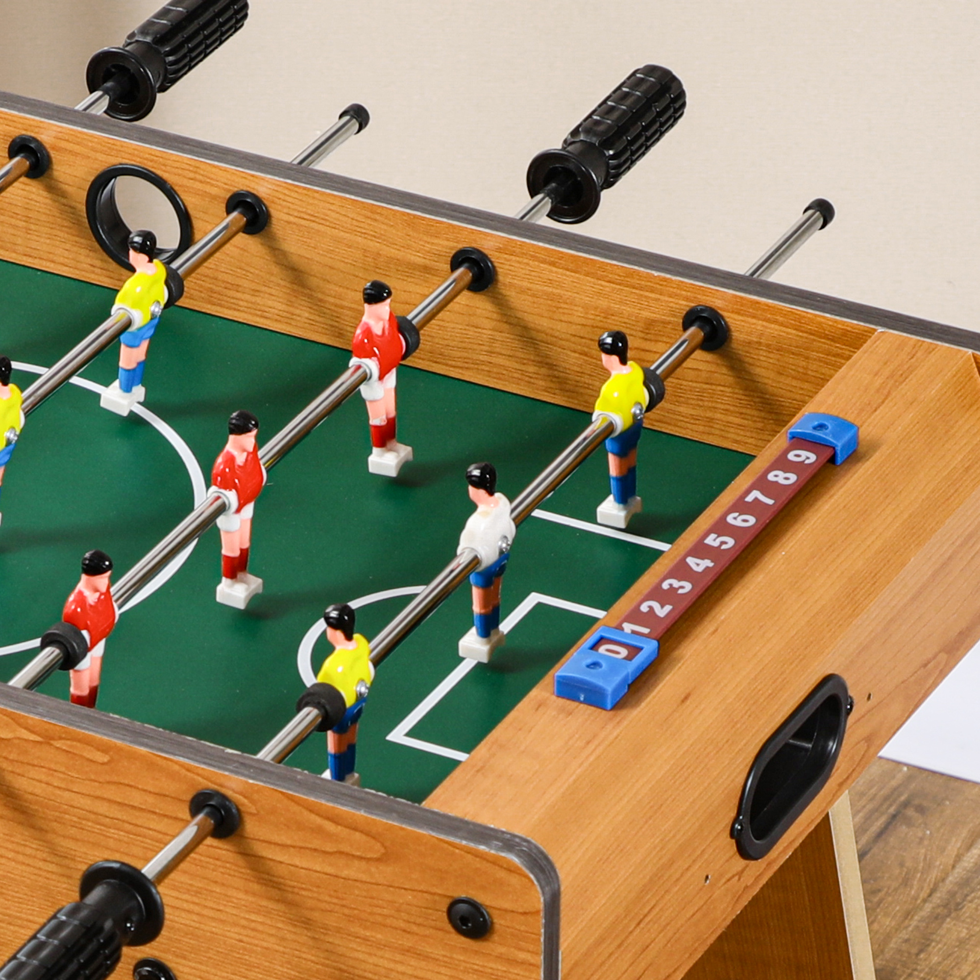 Una mesa de futbolín con jugadores de uniforme amarillo, rojo y blanco. La mesa tiene un campo verde, madera marrón y un contador de goles.