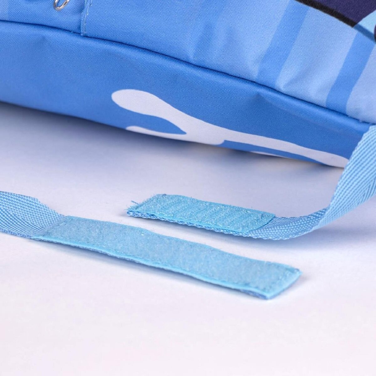 Primer plano de una tela azul con patrones blancos. Se ven dos correas de velcro, una separada. El fondo es blanco liso.