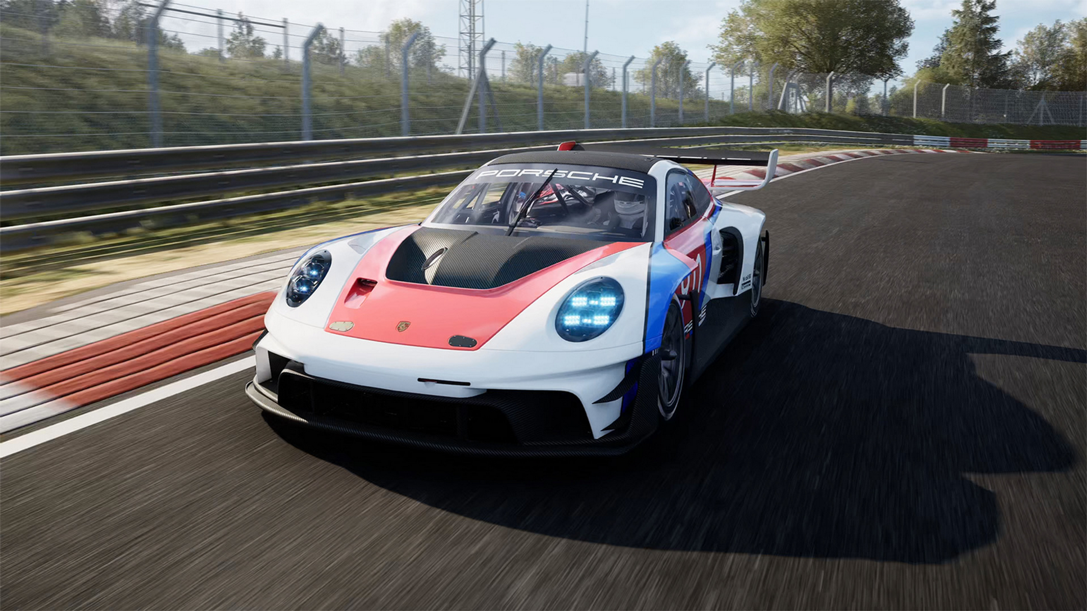 Un'auto da corsa Porsche colorata sfreccia su una pista. L'auto è bianca, rossa e blu. Lo sfondo mostra alberi e una recinzione.