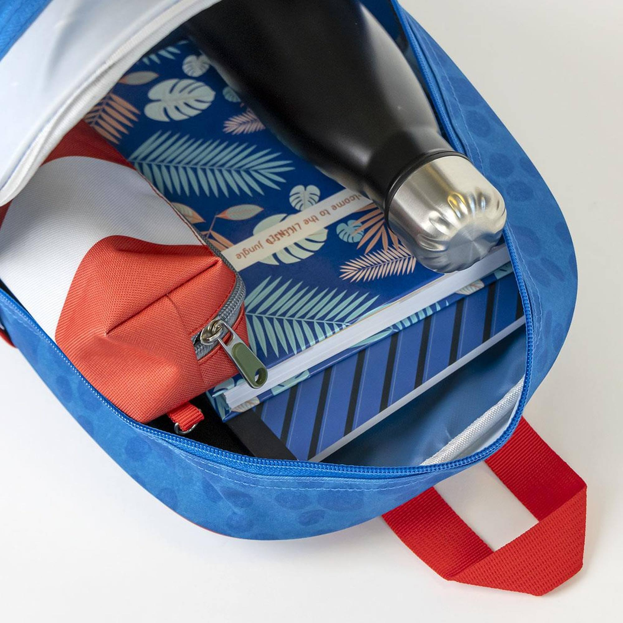 Mochila azul abierta, llena de cuadernos, una botella de agua negra y un estuche rojo y blanco.