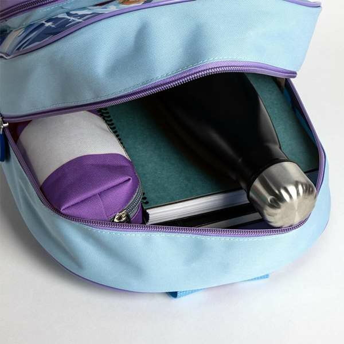 Offener blauer Rucksack mit lila Besatz. Im Inneren sind eine schwarze Wasserflasche, Notizbücher und ein Federmäppchen zu sehen.