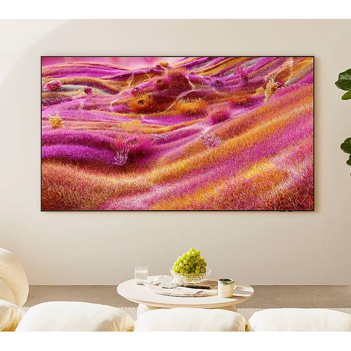 Una TV mostra un paesaggio astratto viola e oro. Un tavolo contiene uva, un bicchiere e una tazza. Sedili beige davanti.