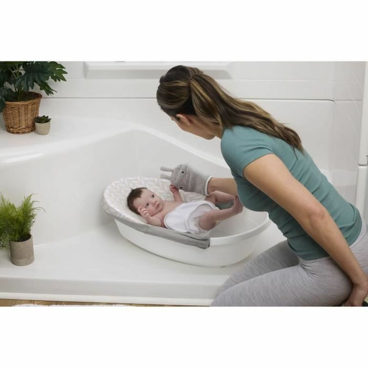 Eine Frau bereitet ein Baby in einer Wanne zum Baden vor. Das Baby liegt in einer Babybadewanne. Ein grauer Waschhandschuh wird benutzt.