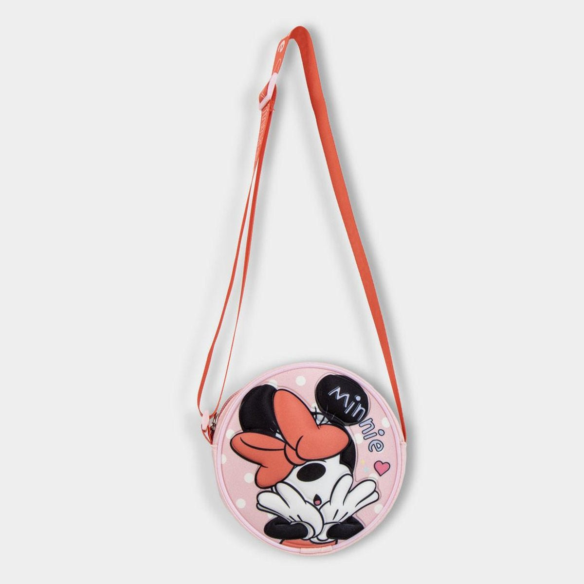 Un bolso rosa de Minnie Mouse con una correa roja cuelga. Tiene forma redonda con lunares y la cara de Minnie.