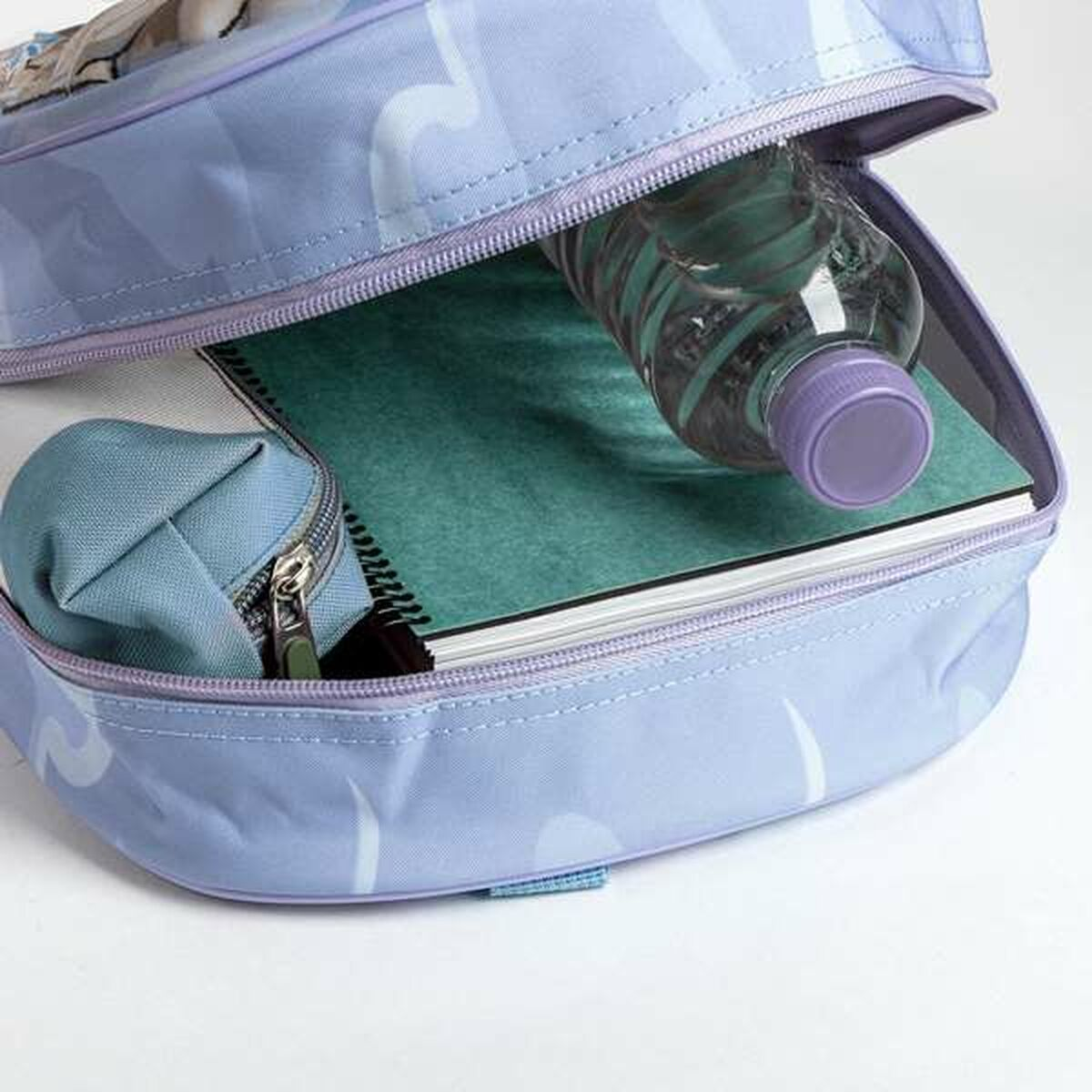 Mochila azul abierta con botella de agua, cuaderno y estuche. La botella tiene tapa morada. El estuche está con cremallera.