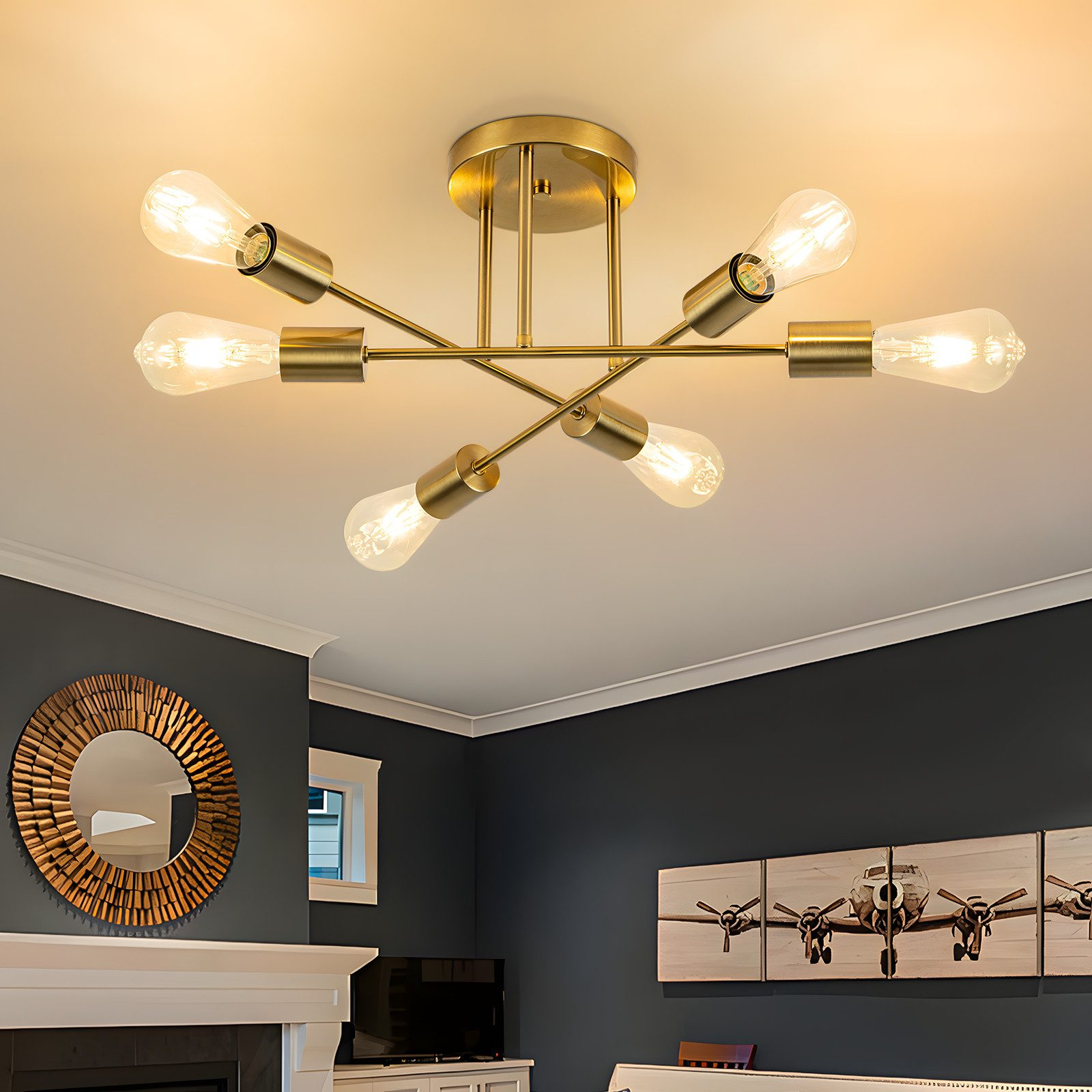 Złota lampa sufitowa z sześcioma żarówkami, lustrem i grafiką samolotu na szarej ścianie.