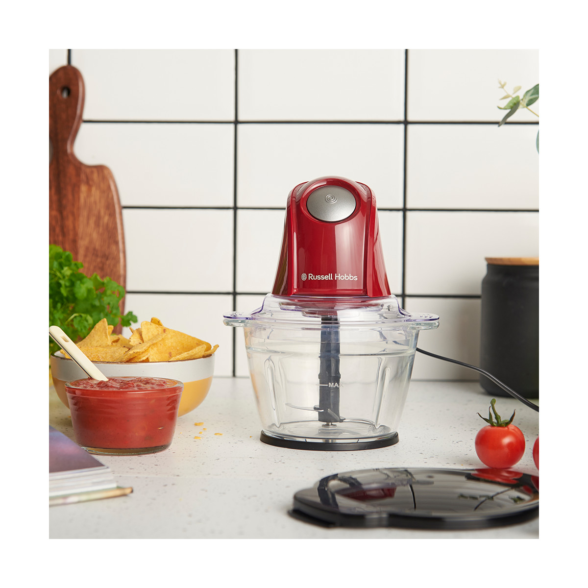 Ein roter Russell Hobbs-Foodprozessor steht auf einer Theke neben Salsa, Chips, Tomaten und einem Schneidebrett.