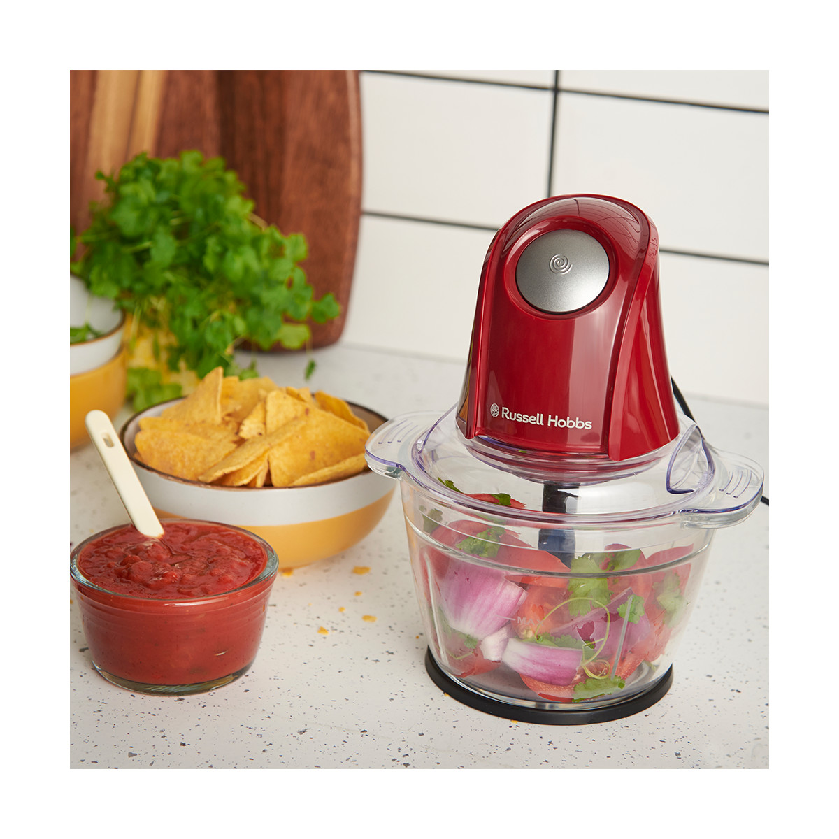 Ein roter Russell Hobbs-Foodprozessor mit gehacktem Gemüse. Salsa, Tortillachips und Koriander sind im Hintergrund.