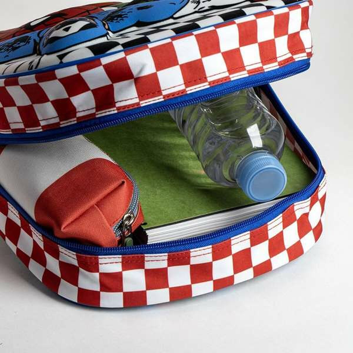 Offene Lunch-Tasche mit rot-weißem Karomuster, einer Wasserflasche und einem Federmäppchen. Im Inneren befindet sich eine grüne Oberfläche und ein Buch.