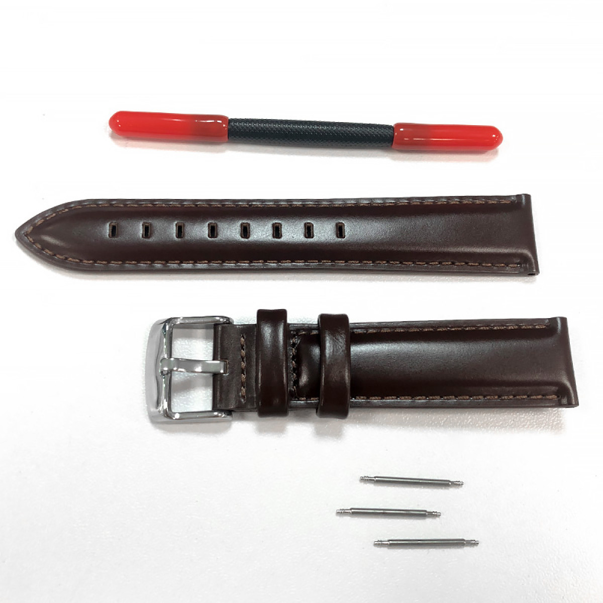 Braunes Lederuhrenarmband, Federstege und ein Werkzeug mit roten Spitzen auf weißer Oberfläche.