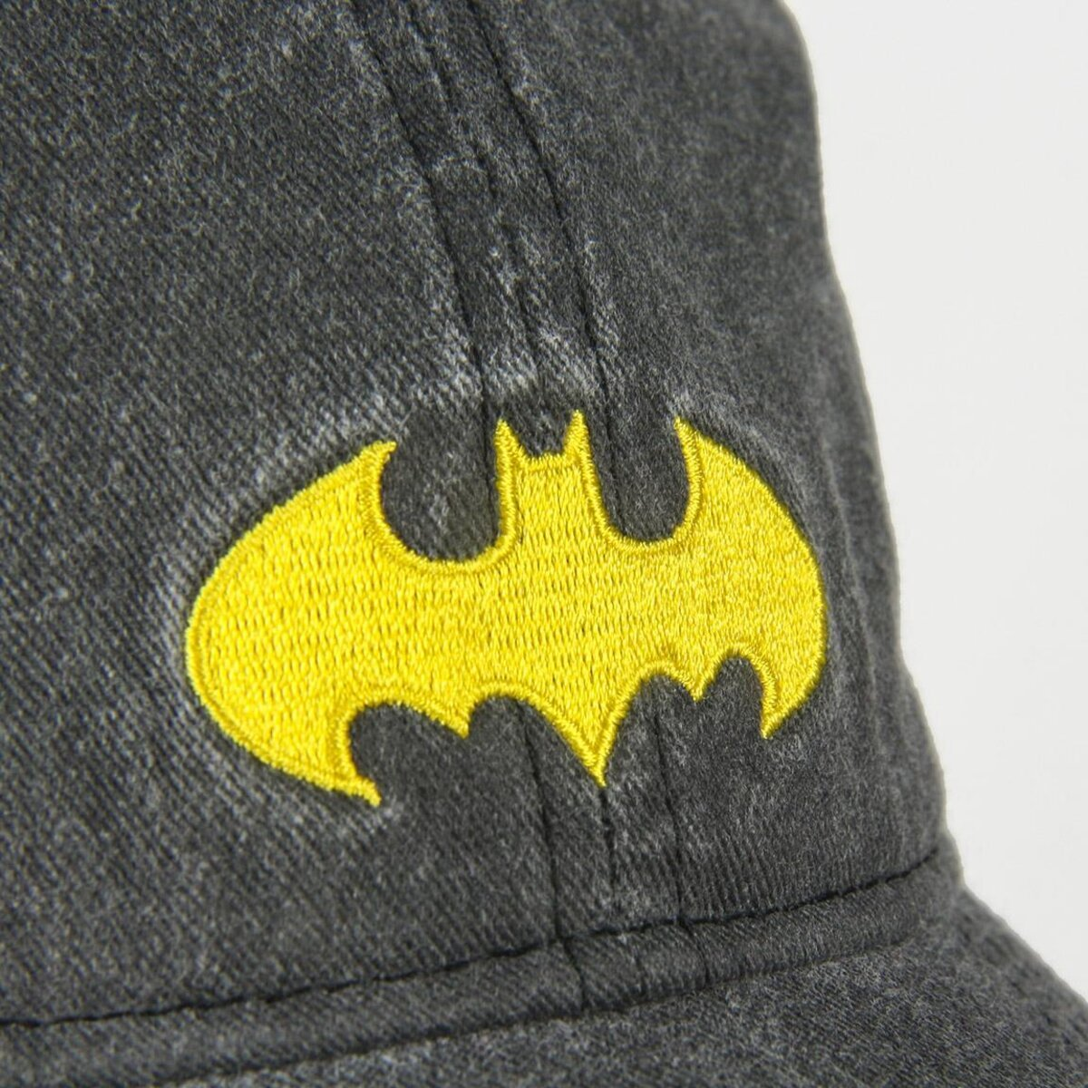 Primer plano de una gorra gris oscuro con el logotipo de Batman bordado en amarillo en la parte delantera. El fondo es blanco.