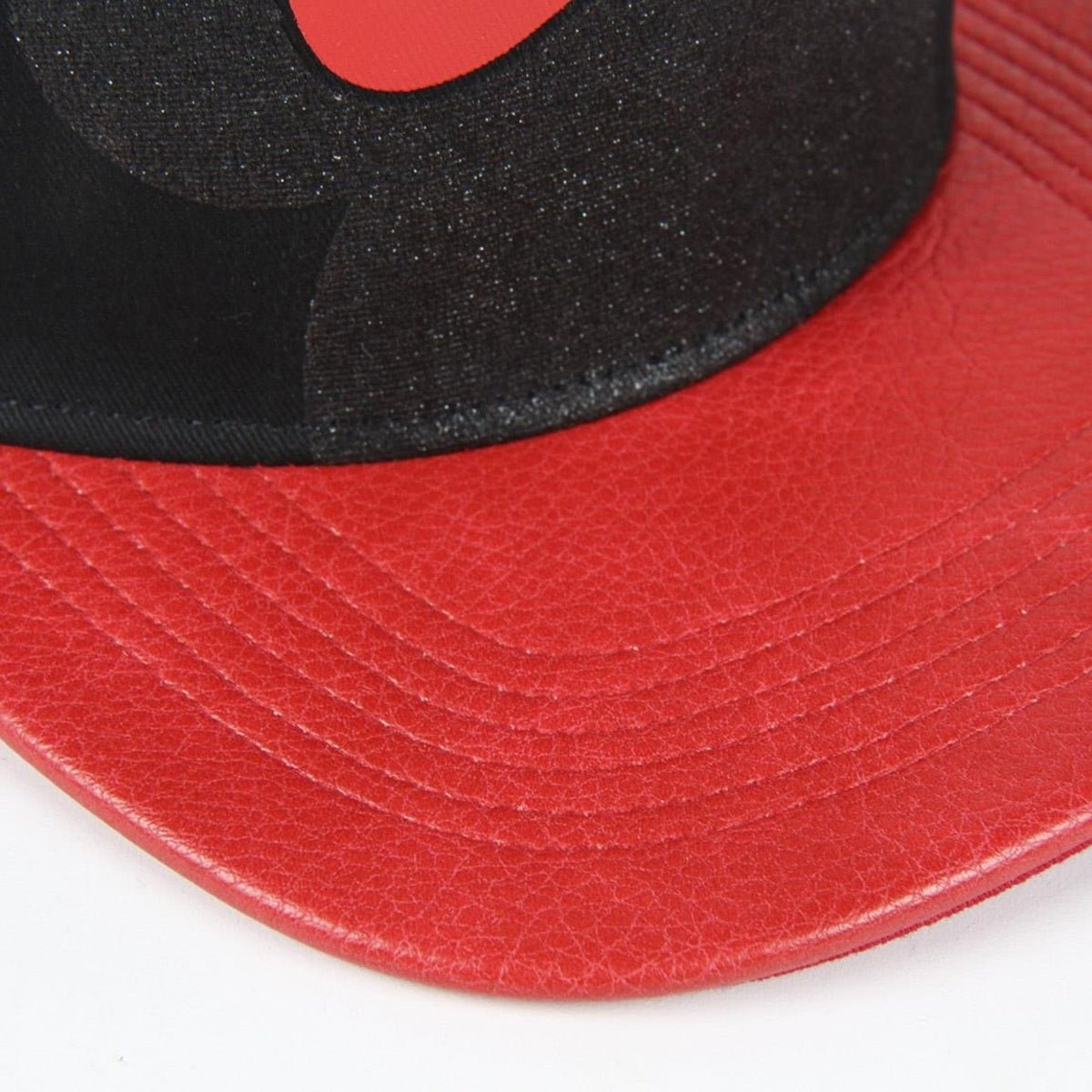 Una gorra roja y negra. La visera es roja, la parte superior es negra con un diseño rojo. El material parece cuero.
