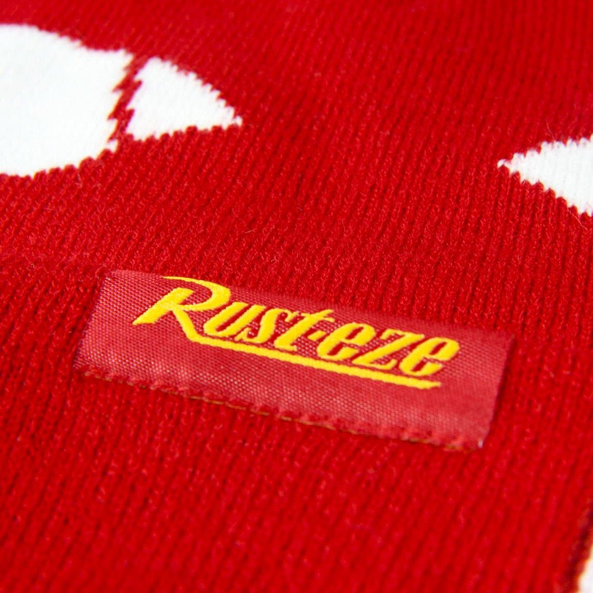 Primer plano de tejido rojo con patrones blancos. Una etiqueta con 'Rusteze' en amarillo cosida en la tela.