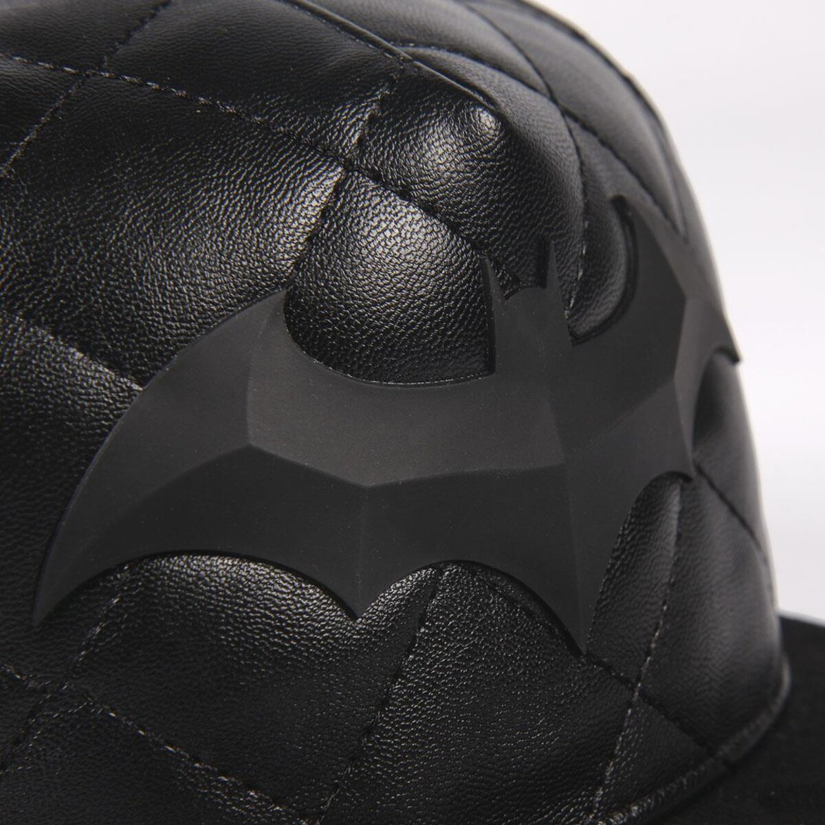 Gorra de béisbol negra con diseño acolchado y el logo negro de Batman. La gorra es de cuero y tiene una visera curva.