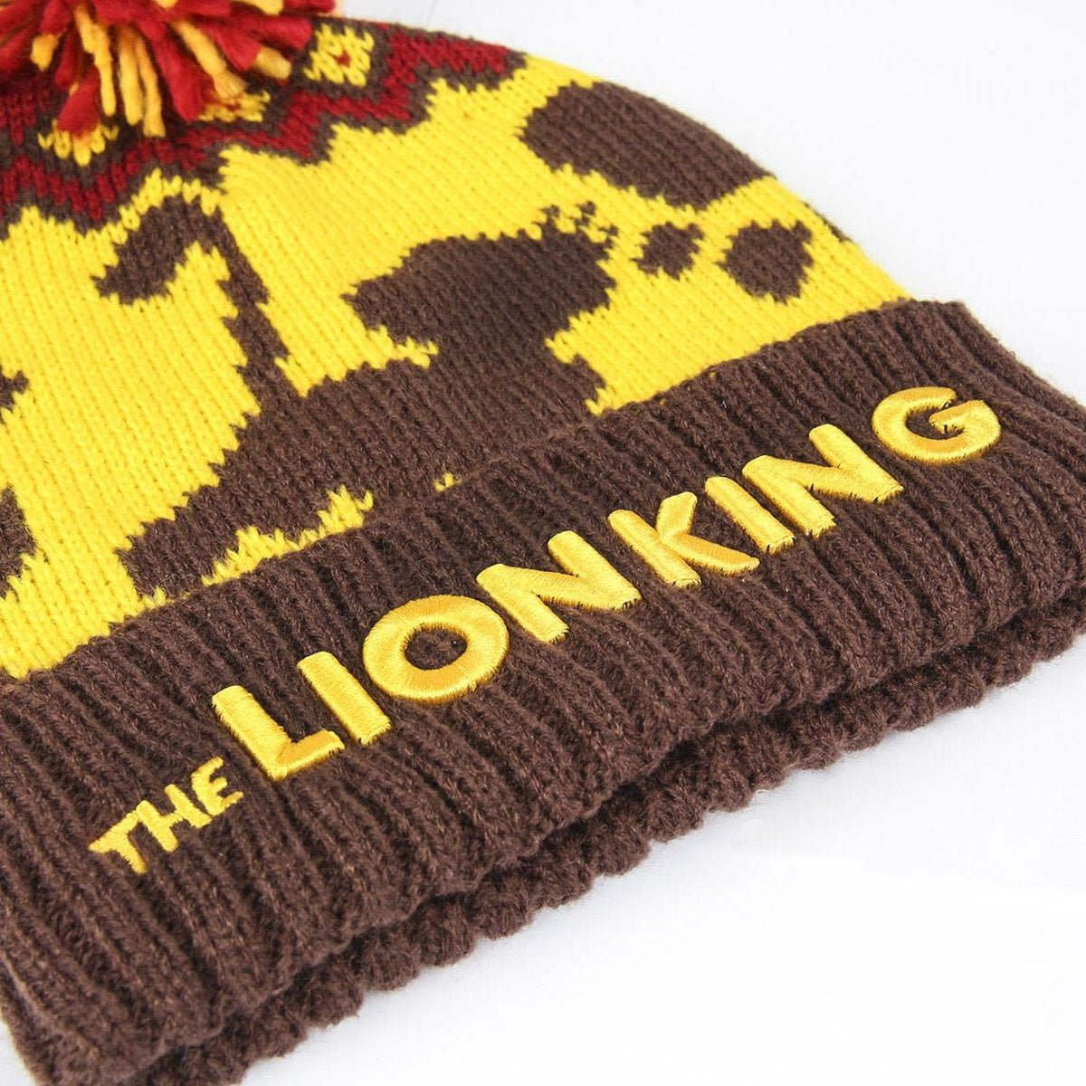 Un gorro marrón con 'THE LION KING' en amarillo. El gorro tiene diseños amarillos y marrones, con un pompón rojo y amarillo.