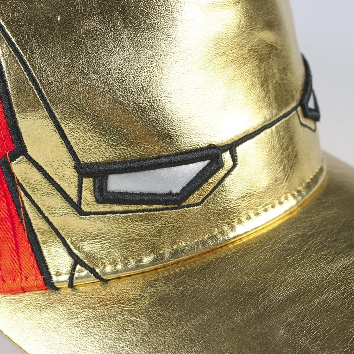 Primer plano de una gorra dorada con un contorno negro de una cara. La gorra tiene una sección roja, ojos blancos y detalles negros.