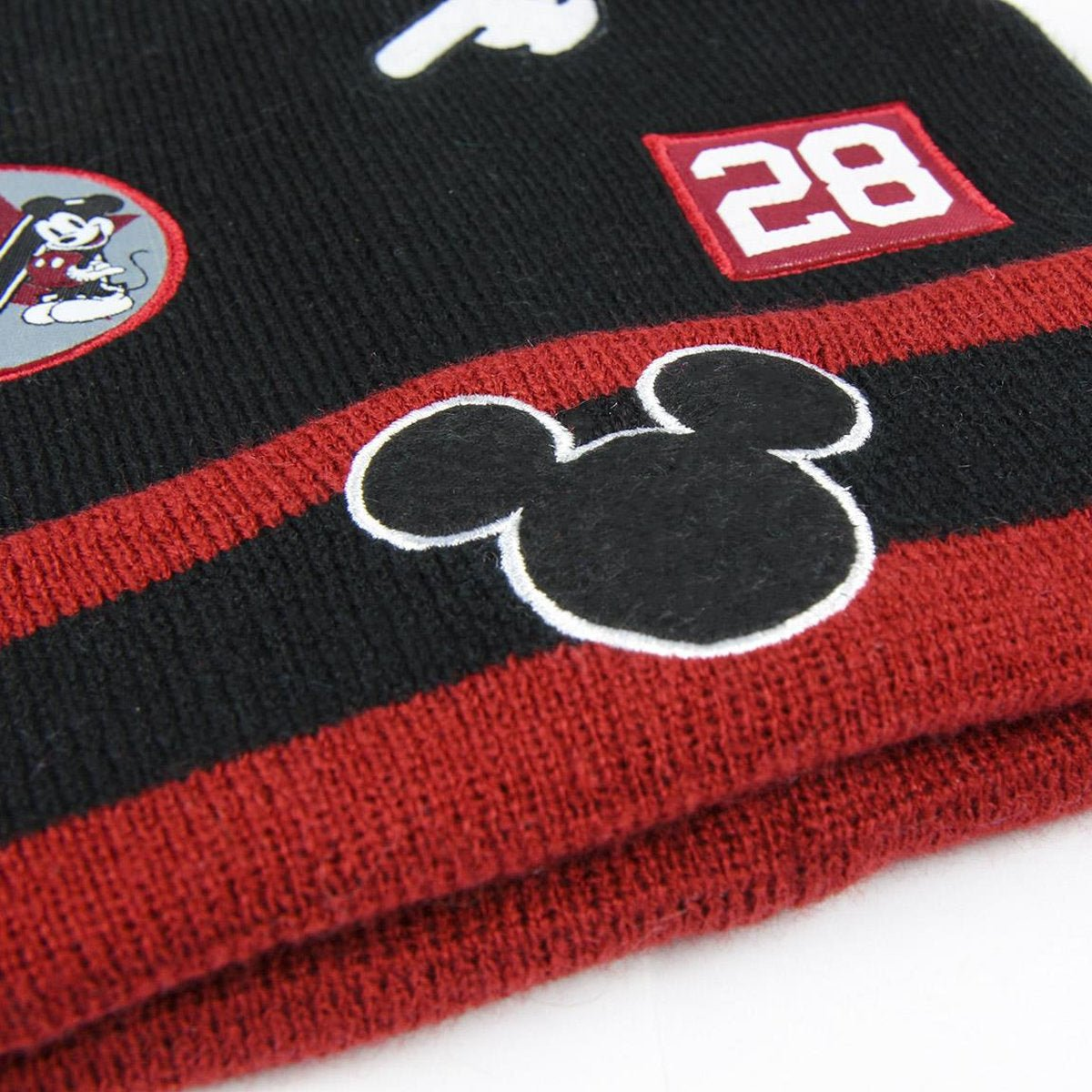 Un gorro negro y rojo con parches de Mickey Mouse y el número 28. El gorro tiene rayas y varios parches temáticos de Disney.