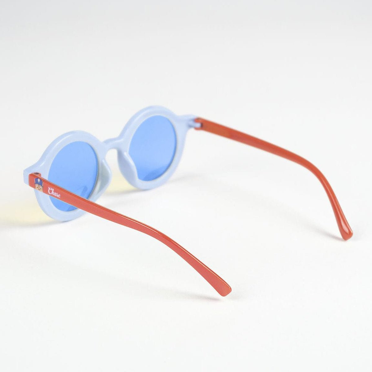 Gafas de sol celeste con montura redonda y lentes azules. Las patillas rojas se extienden desde la montura. El fondo es blanco liso.