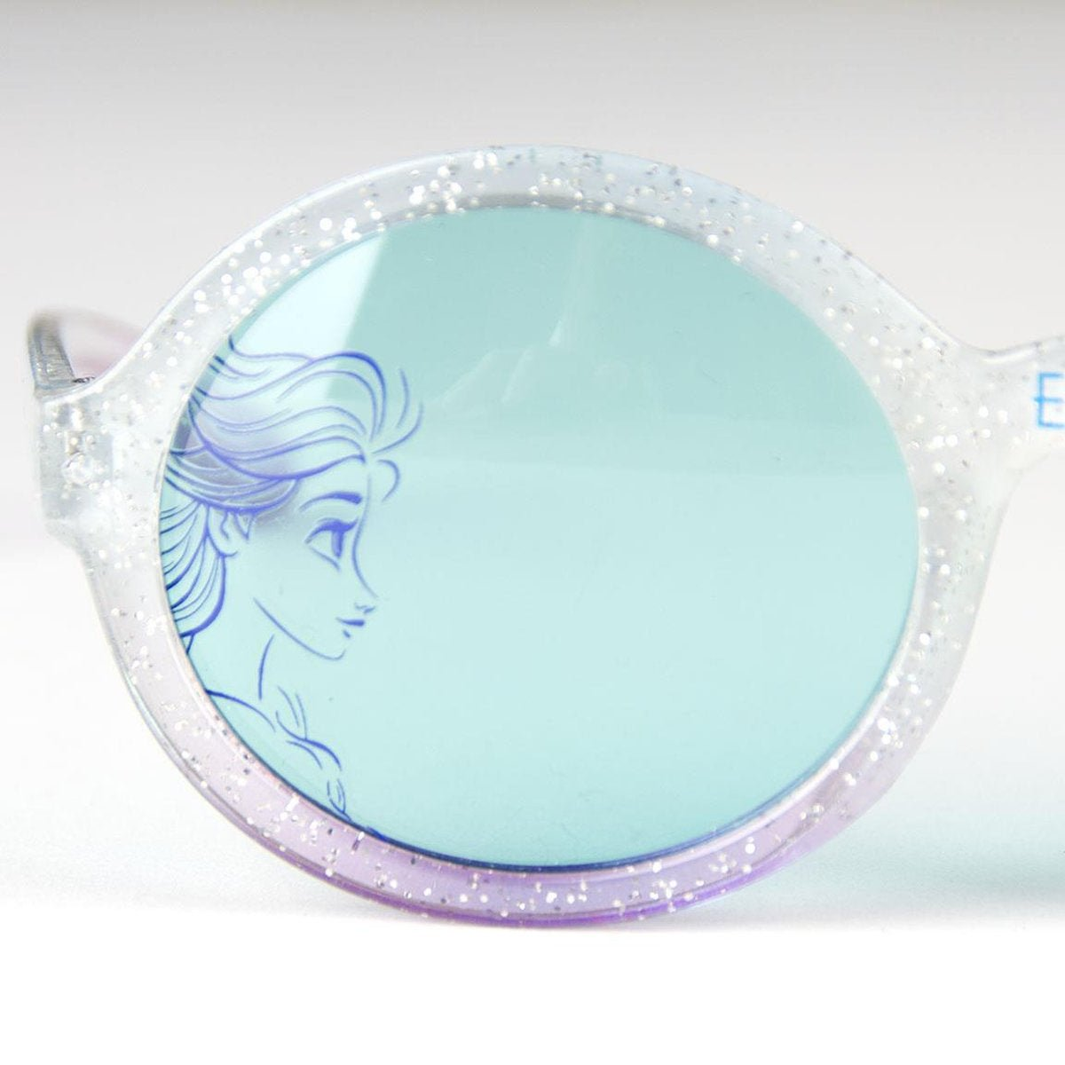 Primer plano de gafas de sol para niños con tinte azul claro. La montura es transparente con purpurina y la lente tiene un contorno de Elsa.