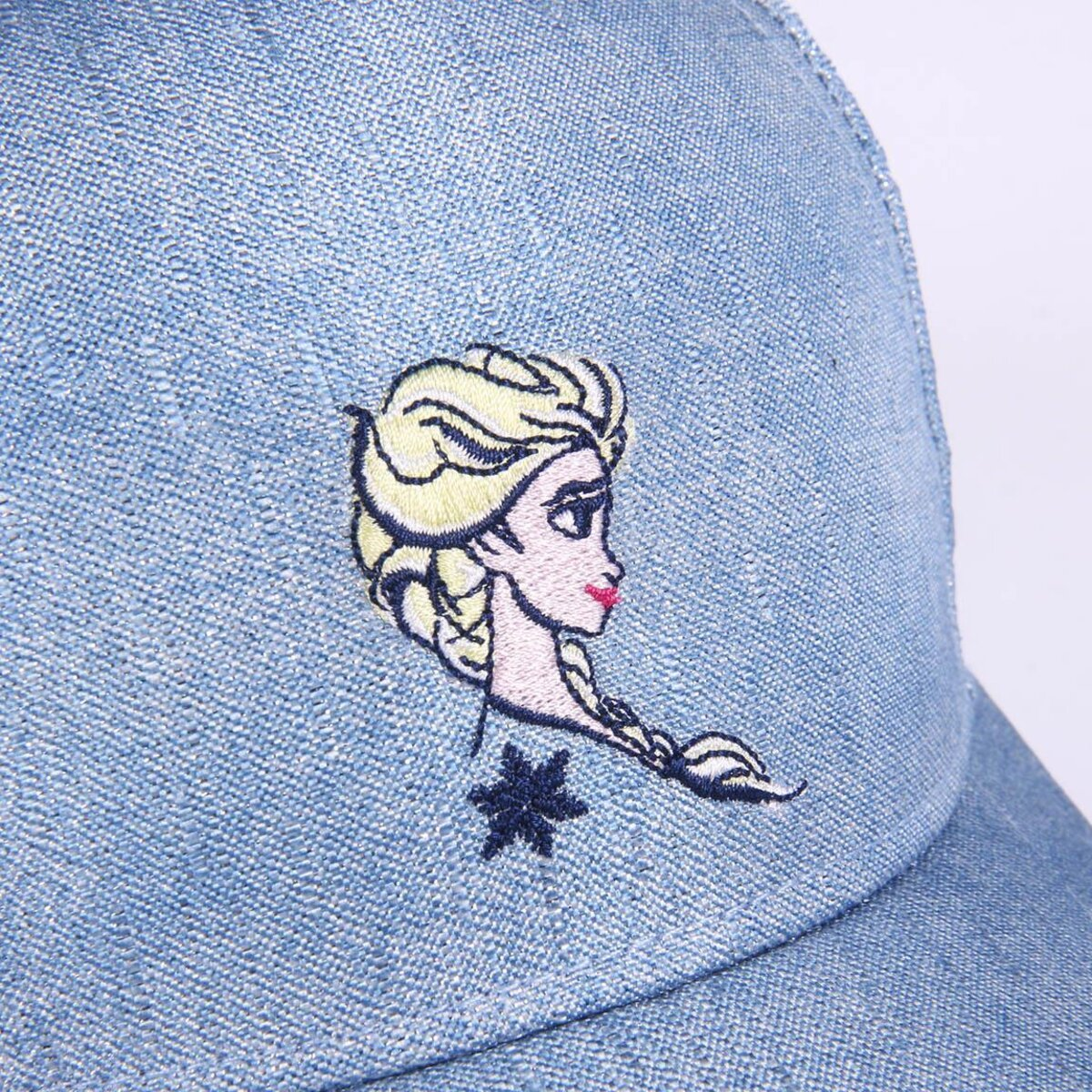 Una gorra de béisbol de mezclilla azul claro presenta una imagen bordada de Elsa de Frozen. La cara, el pelo y un copo de nieve de Elsa son visibles.