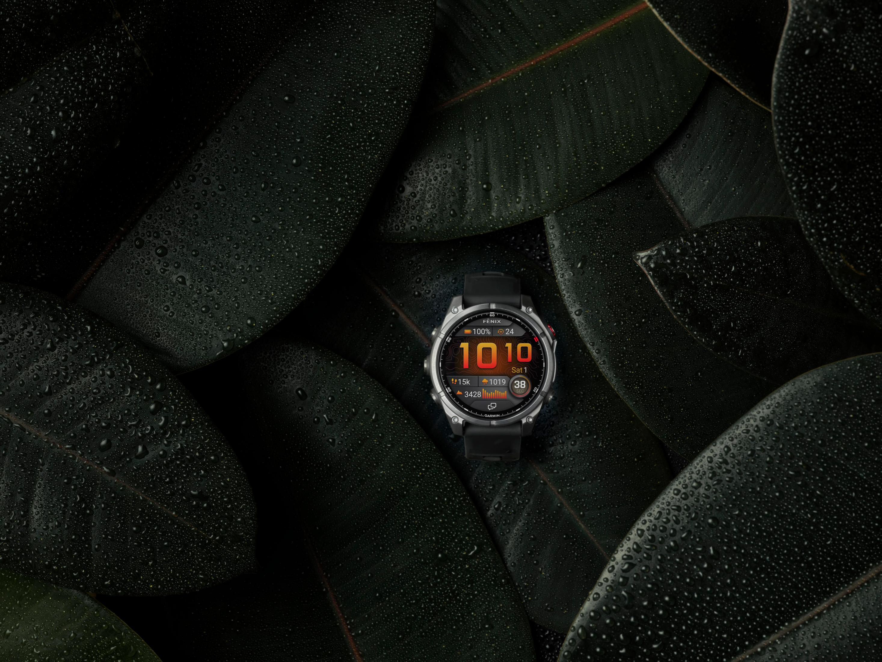 Eine Garmin-Uhr zeigt Zeit und Daten auf dunklen Blättern mit Wassertropfen.