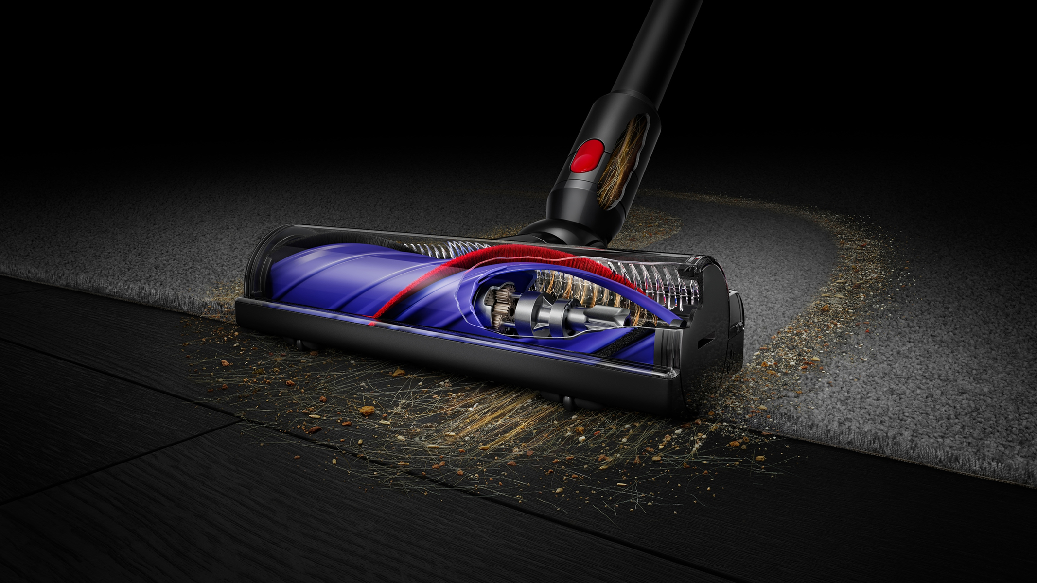 Una testina per aspirapolvere Dyson pulisce un tappeto. Sono presenti componenti interni visibili e particelle di polvere.