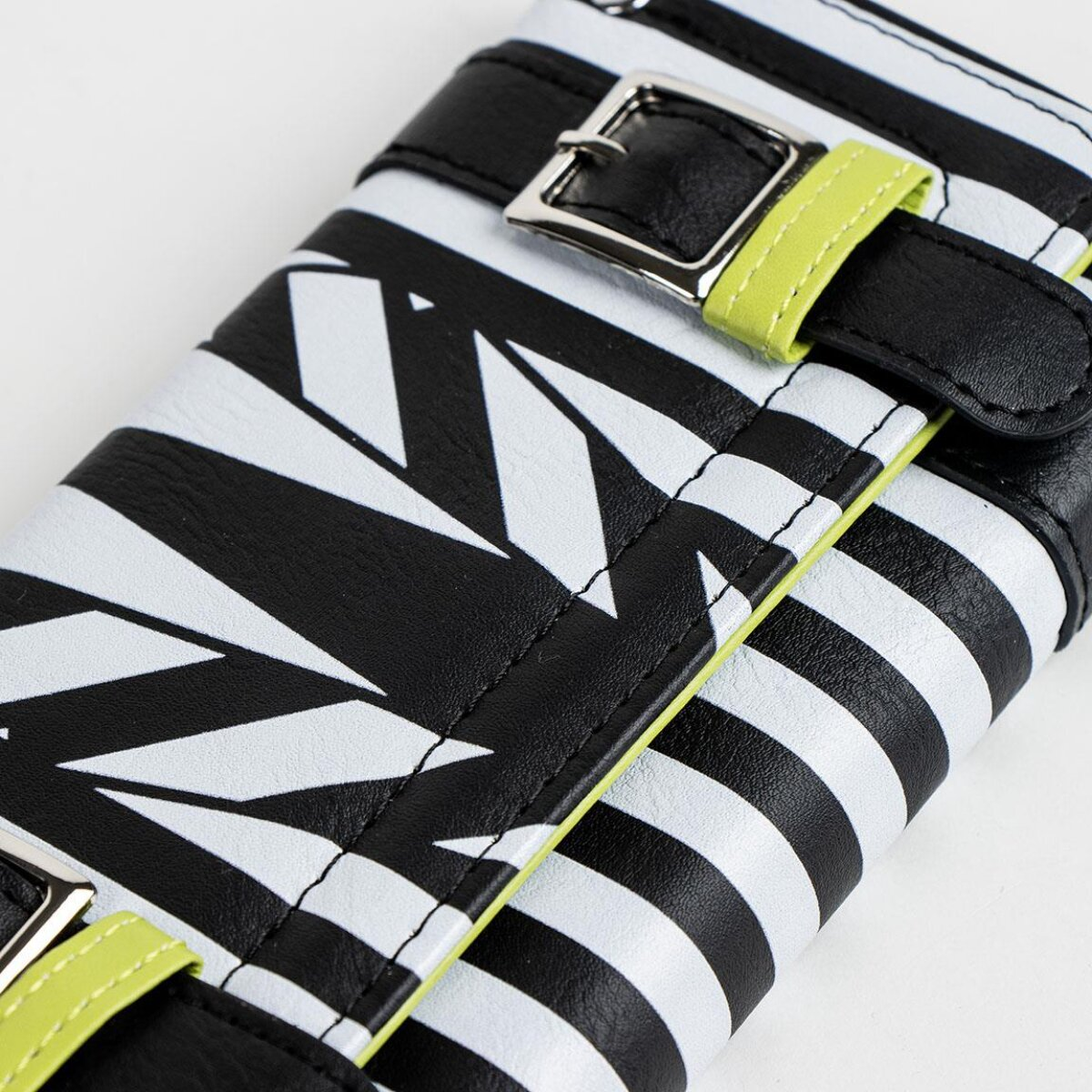 Primer plano de una cartera. La cartera es negra y blanca con patrones de rayas y zig-zag. Presenta un acento verde lima y hebillas metálicas.