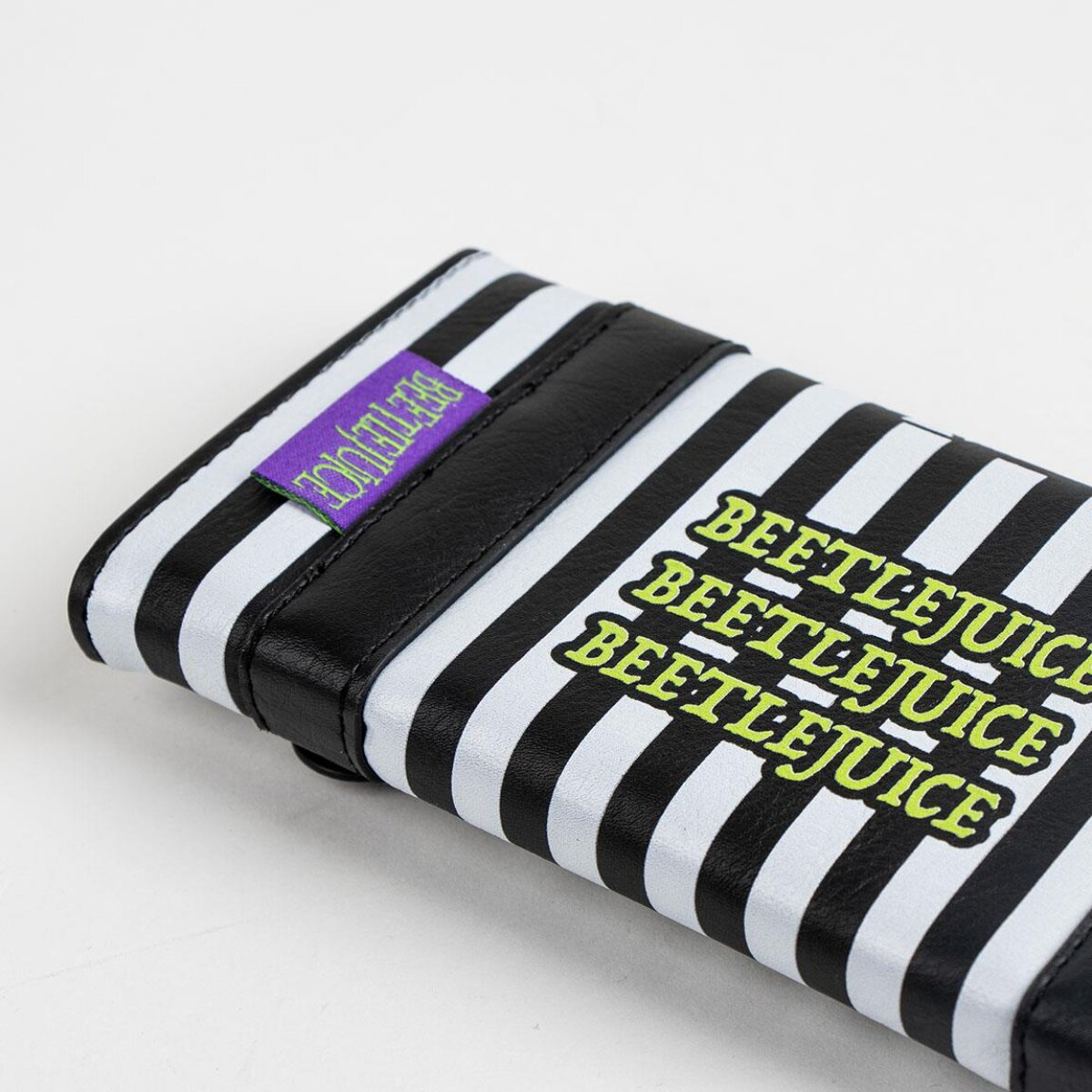 Un accesorio de Beetlejuice a rayas blancas y negras, con la palabra 'Beetlejuice' en letras verdes. También es visible una etiqueta morada.