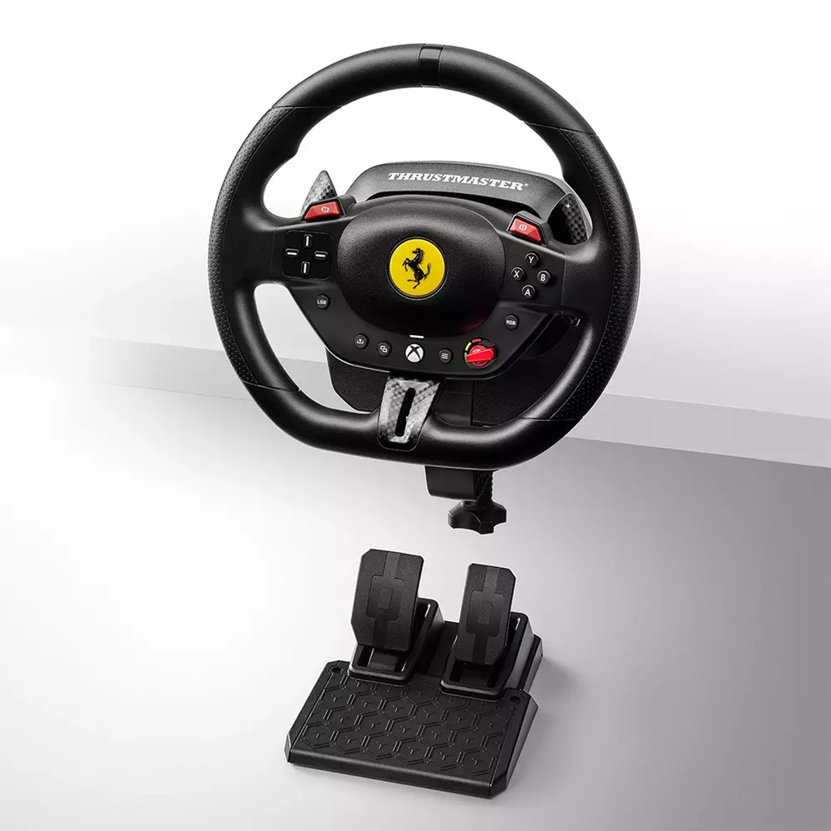 Un juego de volante de carreras Thrustmaster Ferrari negro, que incluye volante y juego de pedales, sobre una superficie blanca.