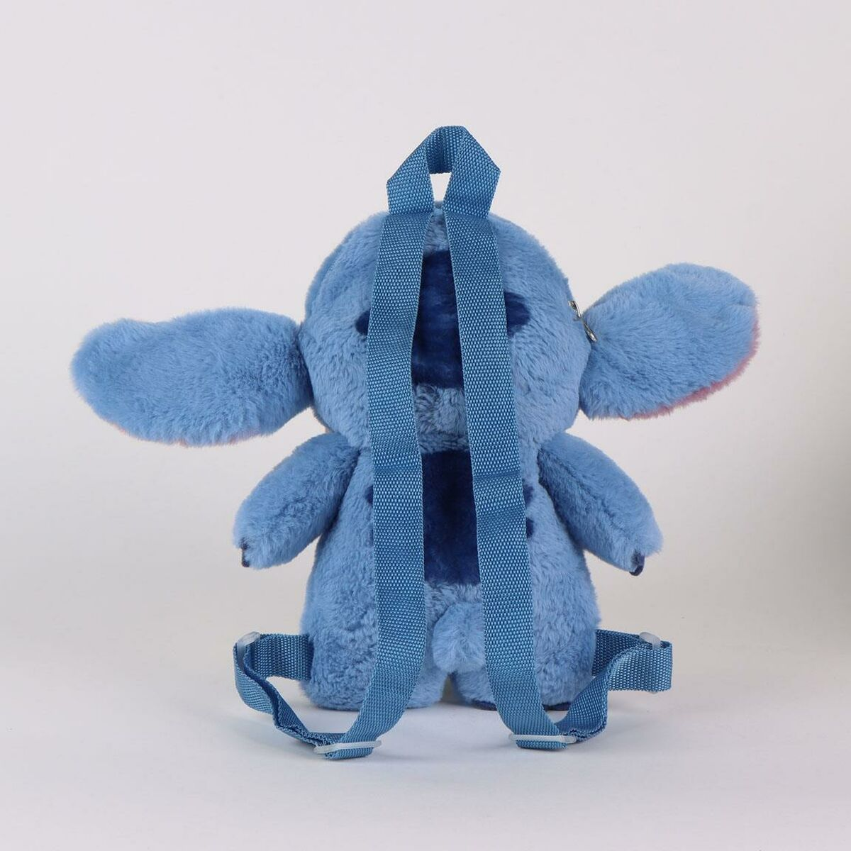 Una mochila de peluche azul de Stitch con correas azules. El peluche tiene orejas grandes, brazos y piernas pequeños y un parche azul oscuro en la espalda.