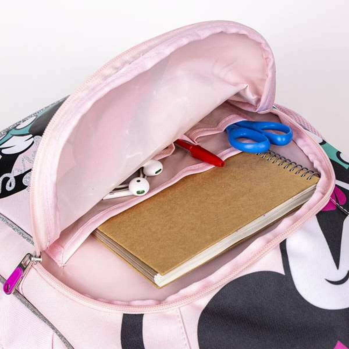 Una mochila rosa está abierta, mostrando un bloc de notas, tijeras, un bolígrafo y auriculares. La mochila tiene un diseño de Minnie Mouse.