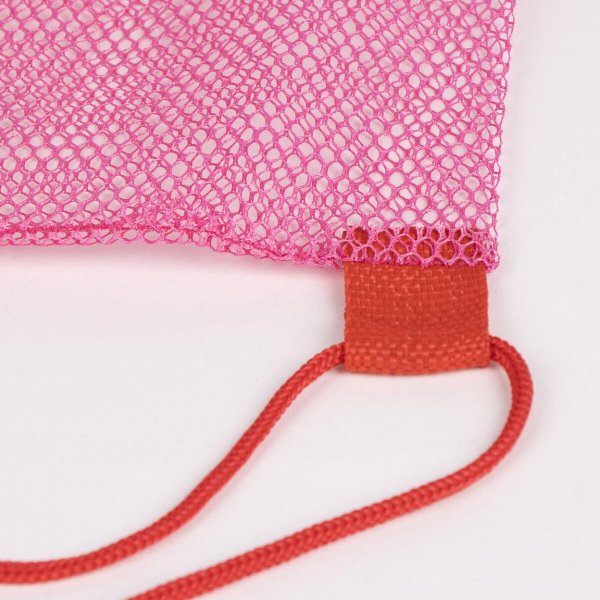 Primer plano de una bolsa de malla rosa con un parche tejido rojo y un cordón rojo. El fondo es blanco.