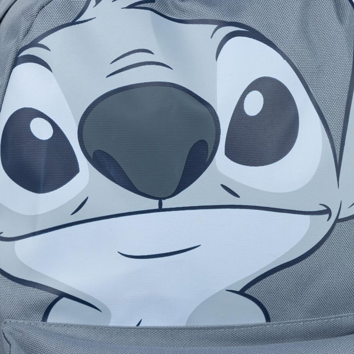 Primer plano de una mochila gris con la cara de Stitch. El diseño incluye ojos grandes, nariz y boca sonriente sobre fondo gris claro.