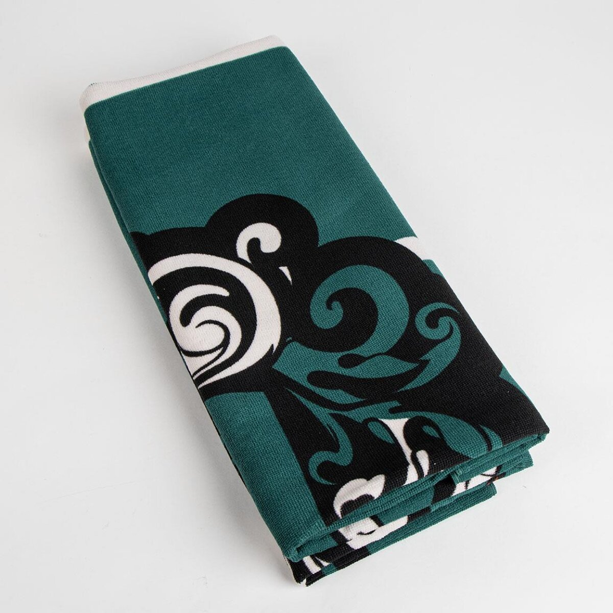 Toalla verde doblada con diseño de remolino negro y blanco. Borde blanco. Fondo blanco liso.