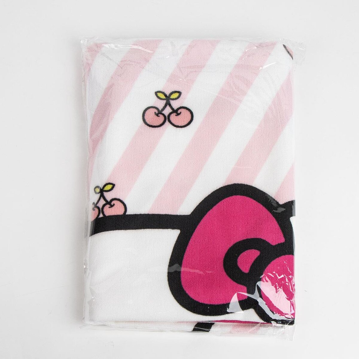 Una toalla doblada en una bolsa transparente, con rayas rosas, cerezas y un gráfico rosa y negro sobre fondo blanco.