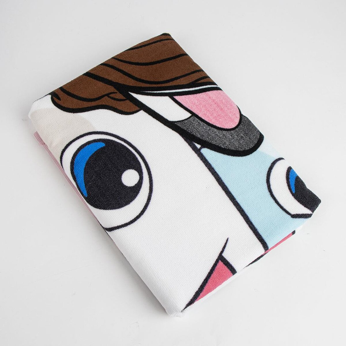 Toalla blanca doblada con diseño de cara de dibujos animados. Presenta ojos grandes, cabello castaño y boca rosa sobre fondo blanco.