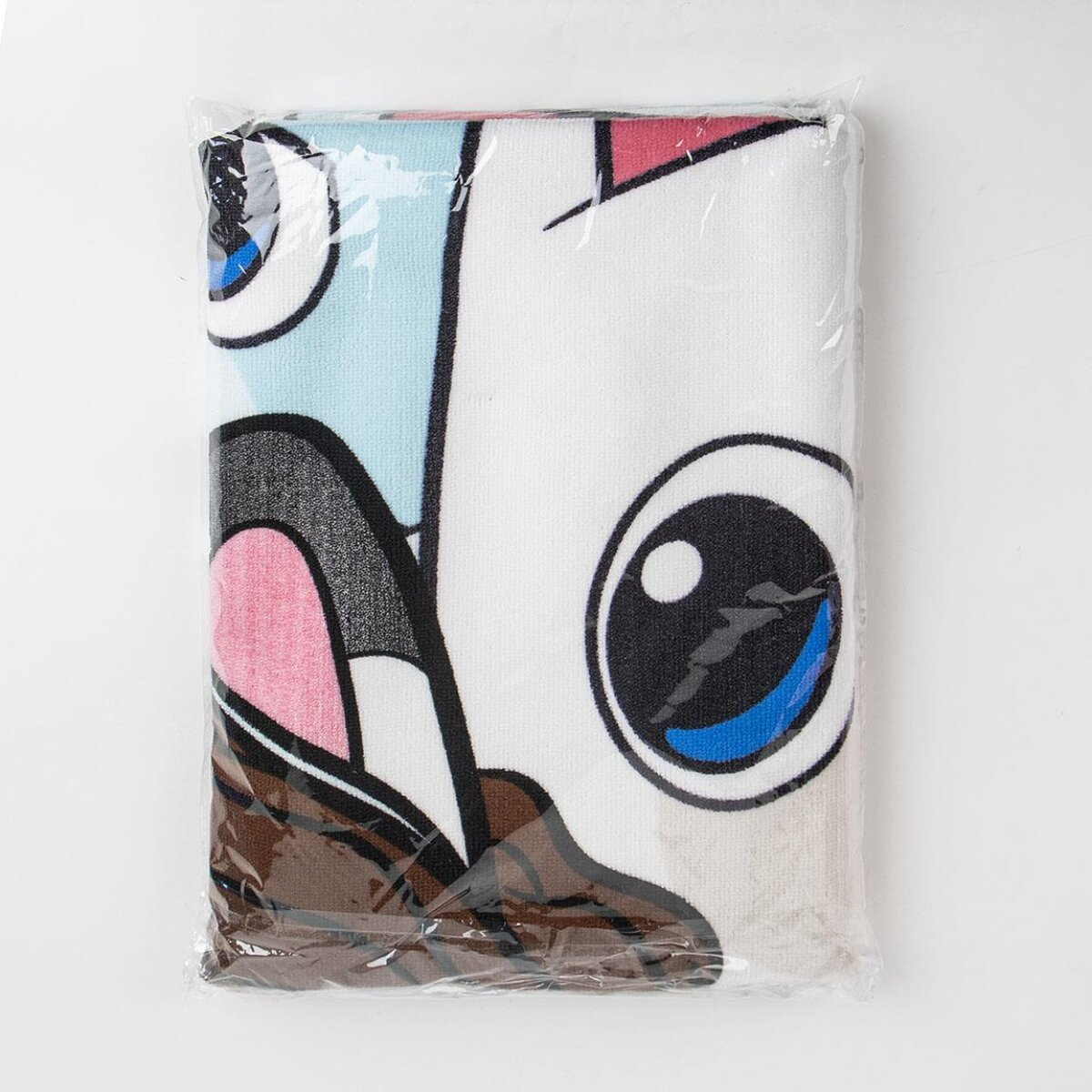 Una toalla con un diseño de cara de dibujos animados dentro de un envoltorio de plástico transparente. La cara tiene ojos grandes, orejas rosas y un área azul claro.