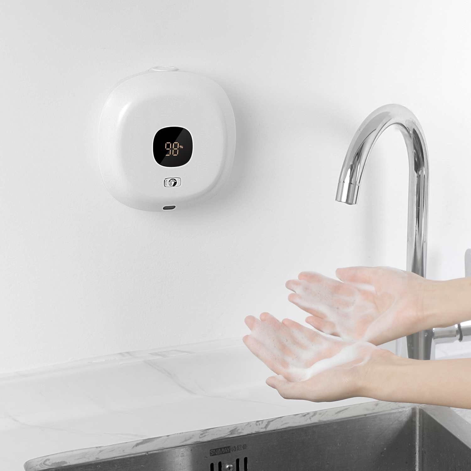 Hände mit Seifenschaum unter einem Wasserhahn. An der Wand befindet sich ein weißer Seifenspender mit Display '98'.
