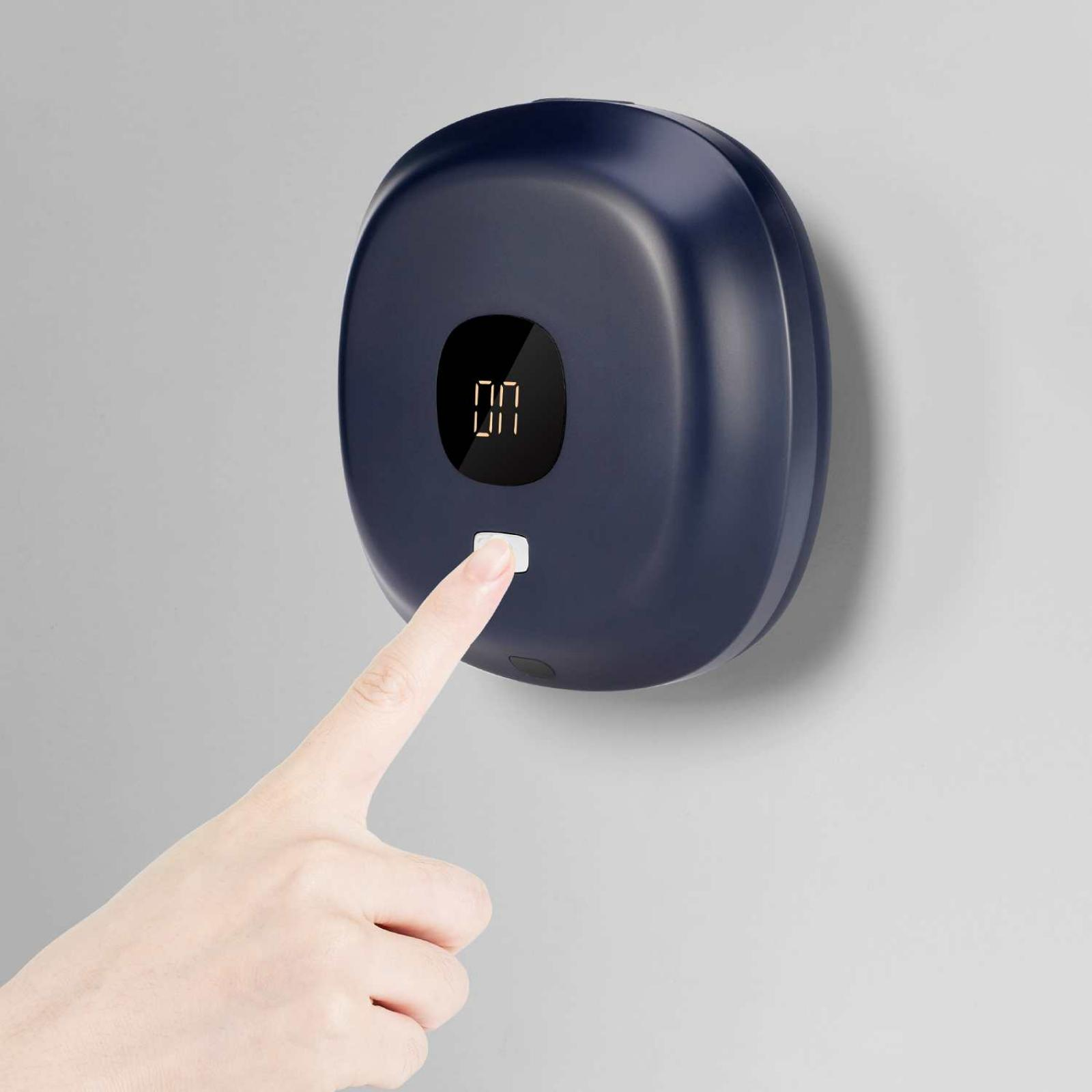 Eine Hand drückt einen weißen Knopf an einem blauen, an der Wand befestigten Gerät. Das Gerät hat ein digitales Display.