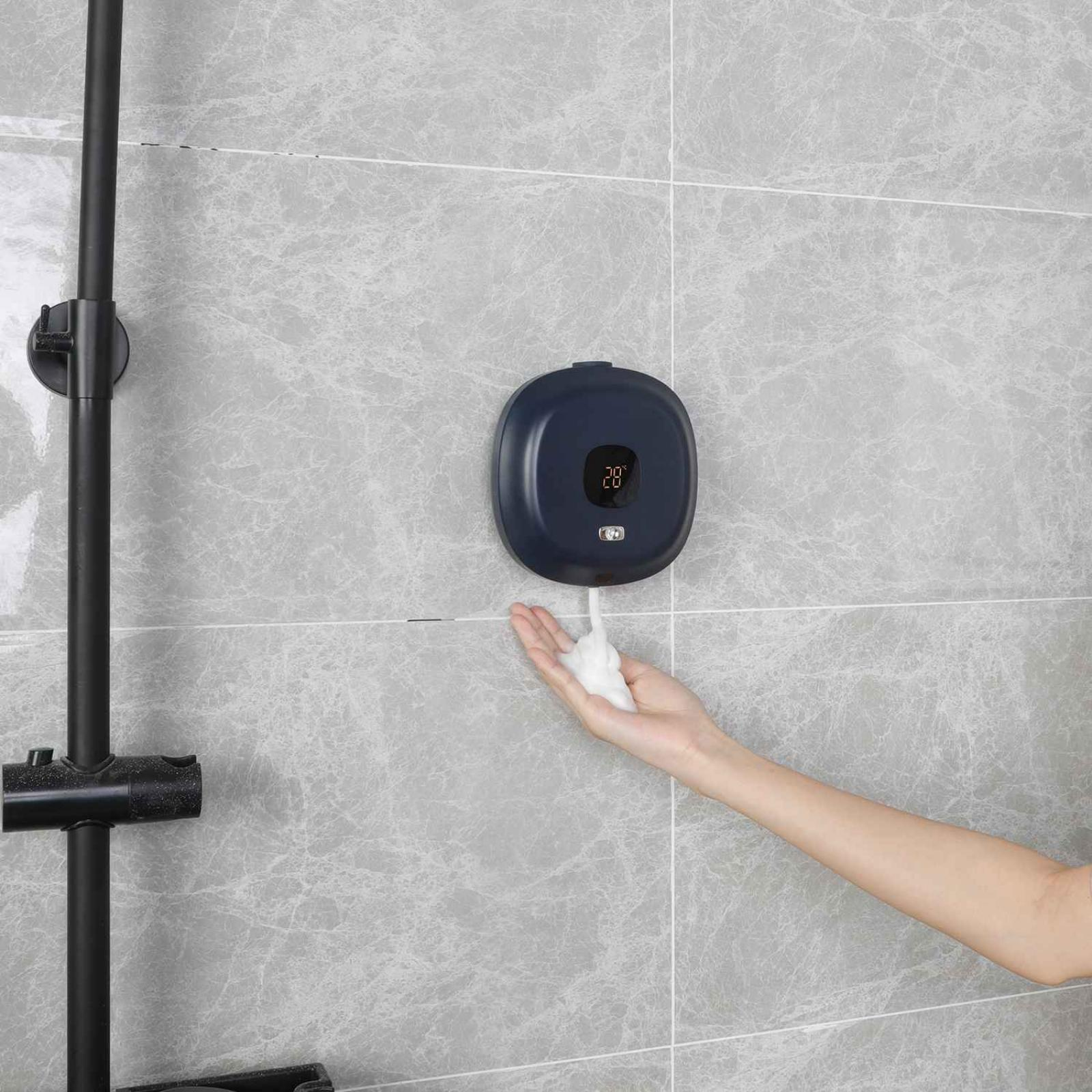 Eine Hand empfängt Seife aus einem blauen Spender. Die Wand ist grau mit schwarzer Duscharmatur.