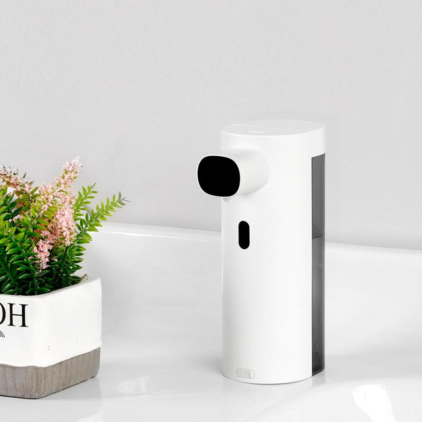 Ein weißer automatischer Seifenspender mit schwarzem Sensor und eine kleine Pflanze in einem Topf stehen auf weißer Oberfläche.