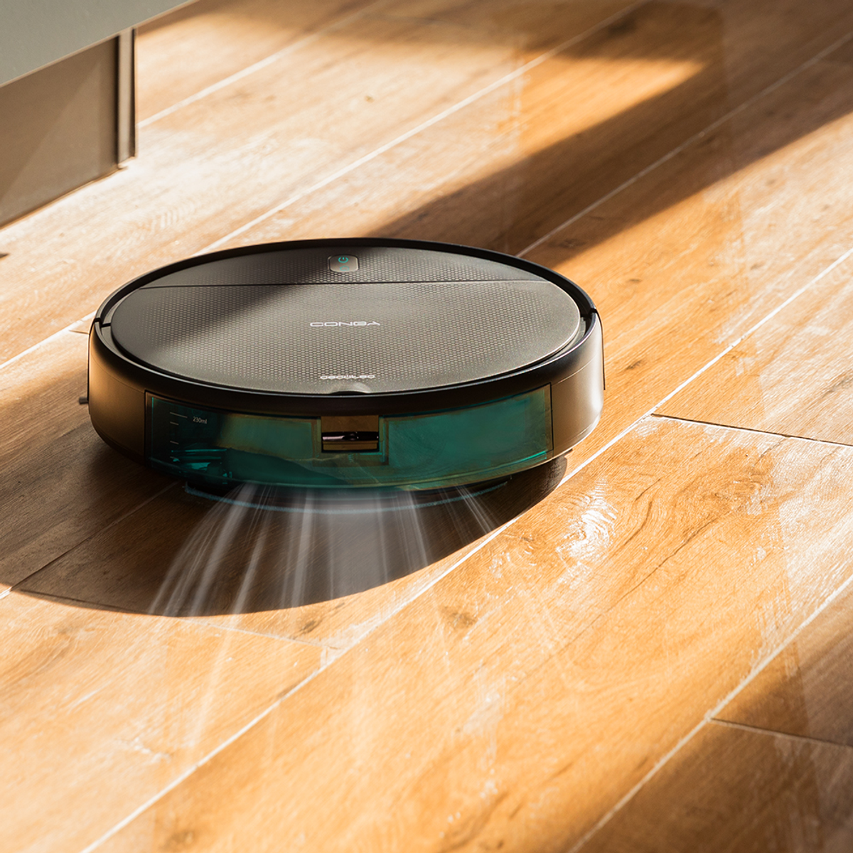 Un aspirapolvere robotico su un pavimento in legno. L'aspirapolvere è nero e verde acqua, emettendo aria. La luce solare proietta ombre.
