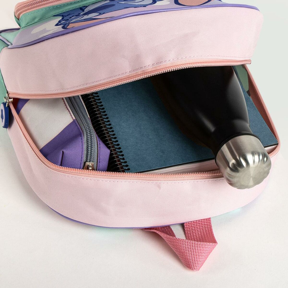 Mochila abierta con cuaderno, botella de agua y estuche. La mochila es rosa y tiene un diseño de Stitch.