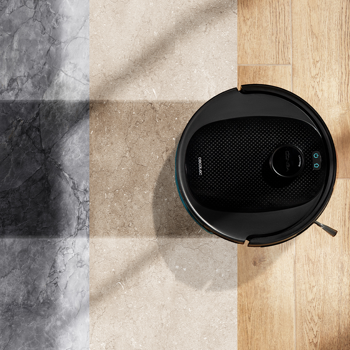 Un aspirapolvere robot nero su un pavimento con tre diverse trame: marmo, pietra beige e pannelli di legno.