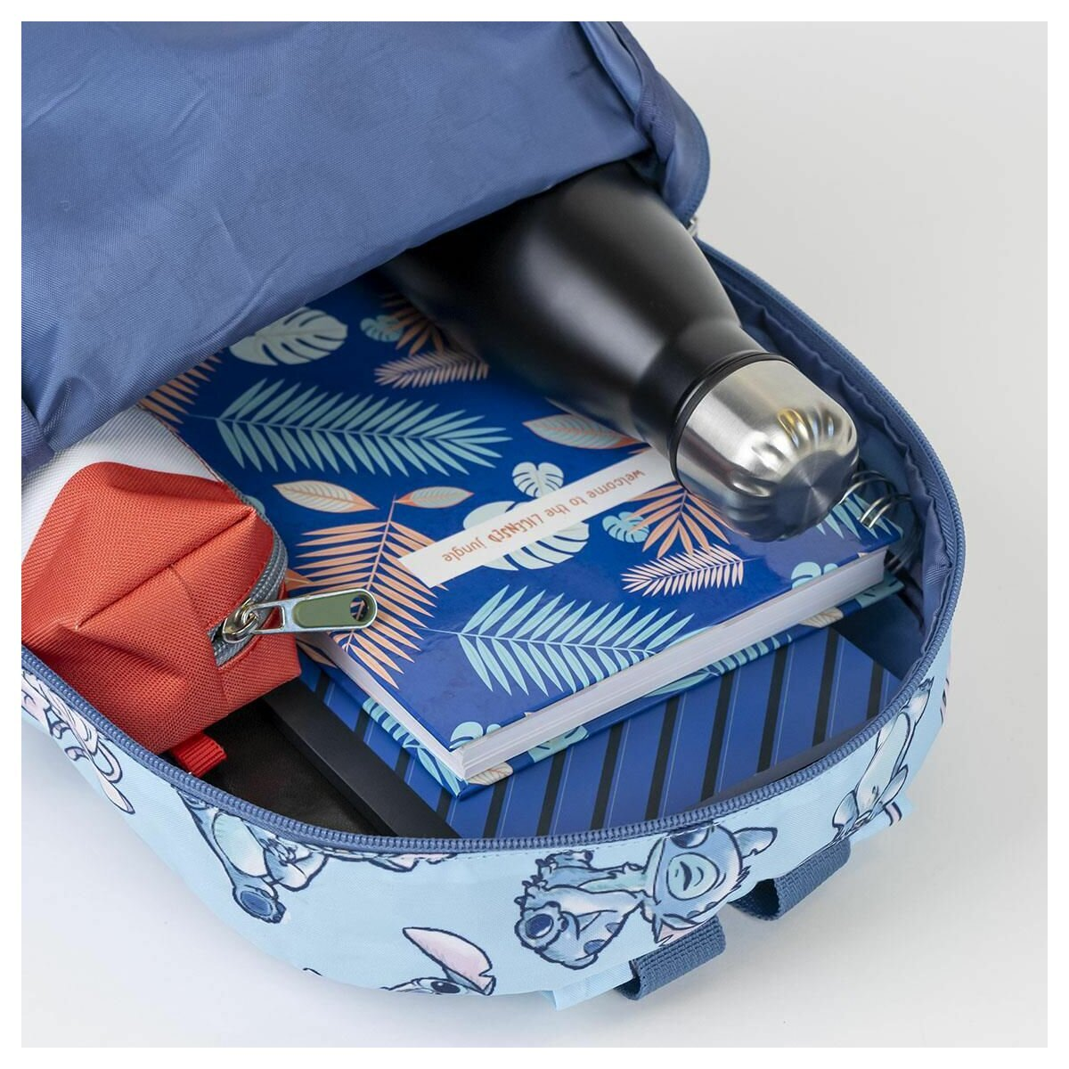 Mochila abierta con una botella de agua negra, un cuaderno y una pequeña bolsa roja. La mochila tiene un estampado de Stitch.