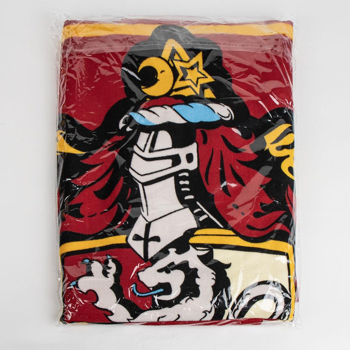 Toalla en envoltorio de plástico. Presenta un diseño con casco de caballero, estrella y león en rojo, negro, amarillo y blanco.